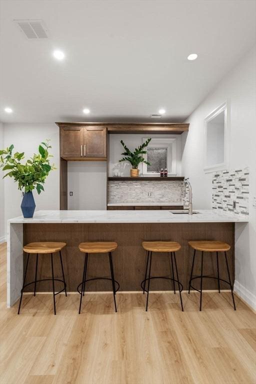 bar featuring sink, backsplash, and light hardwood / wood-style flooring