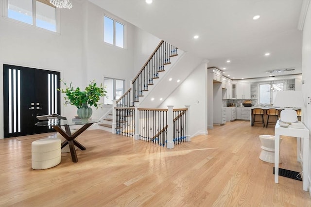 foyer entrance featuring a notable chandelier, a towering ceiling, and light wood-type flooring