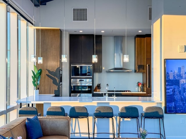 kitchen featuring built in microwave, a towering ceiling, oven, and wall chimney range hood