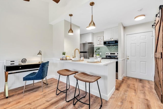 kitchen featuring stainless steel appliances, a barn door, a peninsula, a breakfast bar, and white cabinets