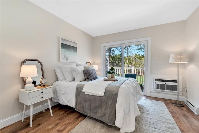 bedroom featuring access to outside, wood finished floors, baseboards, and a wall unit AC