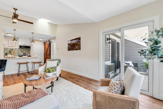living room with light wood-style flooring, ceiling fan, a wainscoted wall, lofted ceiling, and baseboards