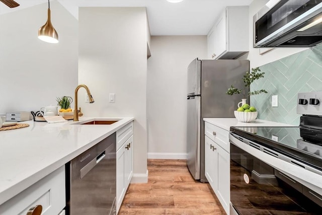 kitchen with stainless steel appliances, a sink, decorative backsplash, light wood finished floors, and hanging light fixtures