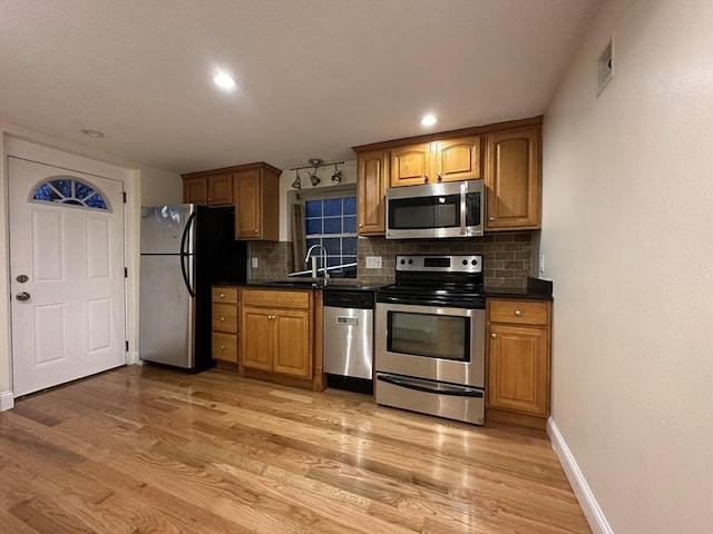 kitchen with light wood-style floors, appliances with stainless steel finishes, a sink, and dark countertops