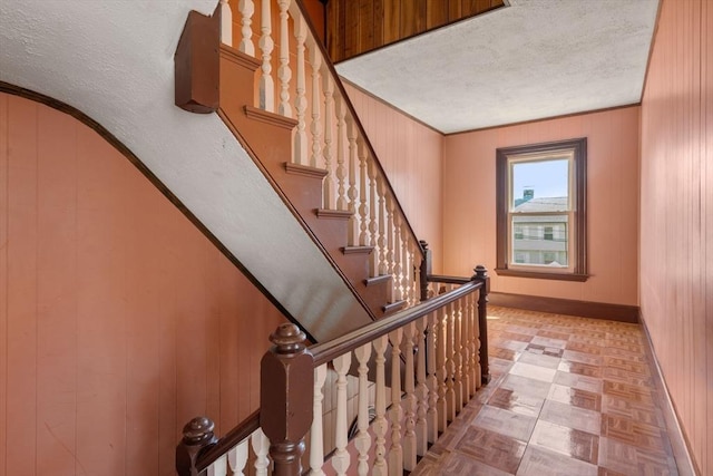 stairway featuring ornamental molding, baseboards, wood walls, and a textured ceiling