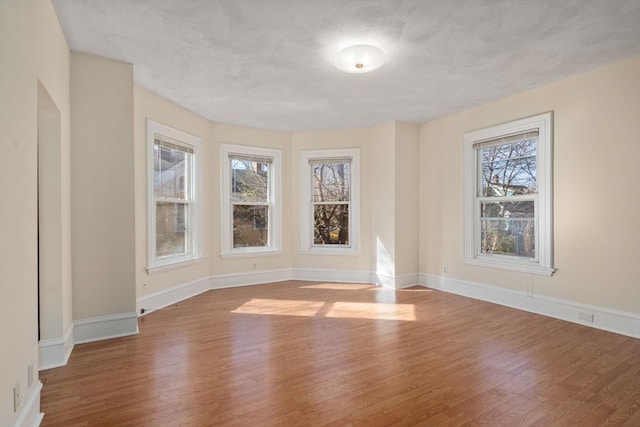 spare room featuring a wealth of natural light, baseboards, a textured ceiling, and wood finished floors