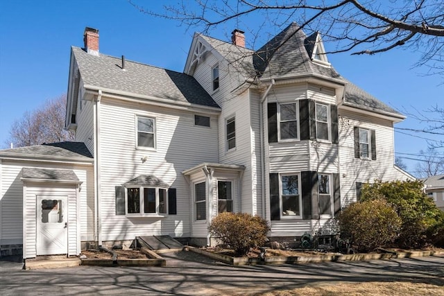 rear view of property with a chimney and a shingled roof