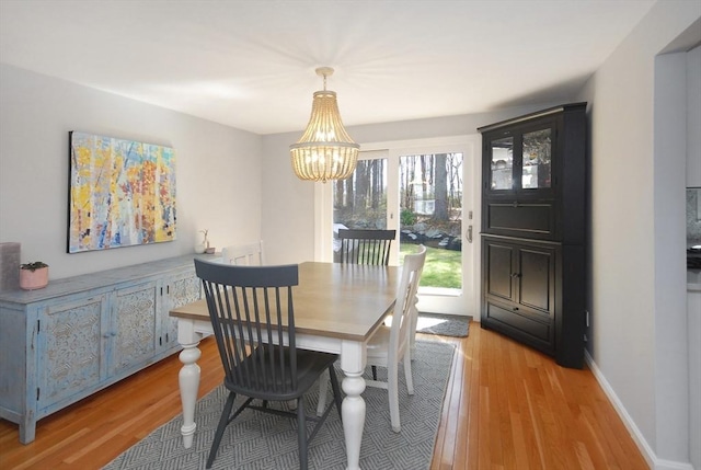 dining area with baseboards, an inviting chandelier, and light wood-style flooring