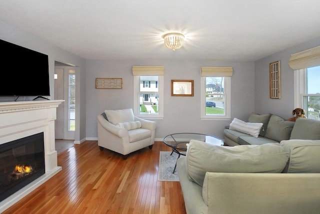 living area featuring baseboards, a glass covered fireplace, and light wood finished floors