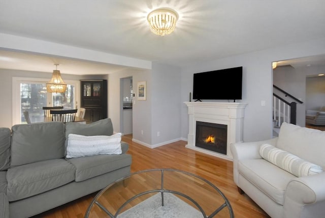 living area with stairs, baseboards, a lit fireplace, a chandelier, and light wood finished floors