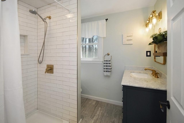 full bathroom with vanity, baseboards, wood finished floors, and a tile shower