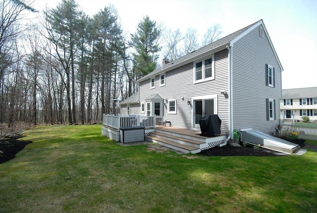 back of property featuring fence, a wooden deck, a chimney, and a yard