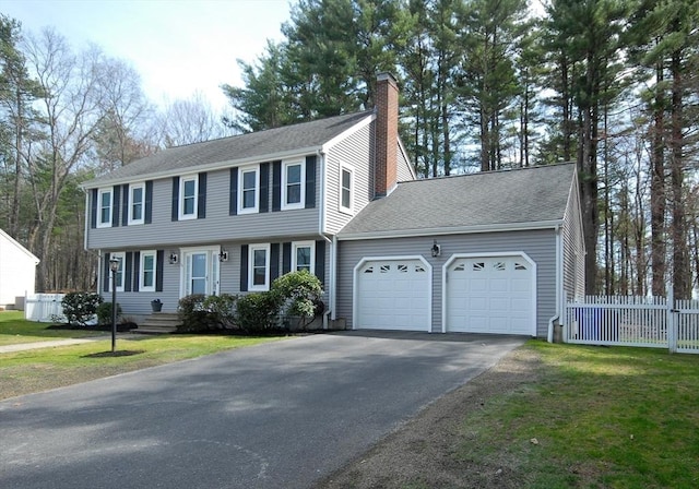 colonial house with a chimney, a front yard, fence, aphalt driveway, and an attached garage
