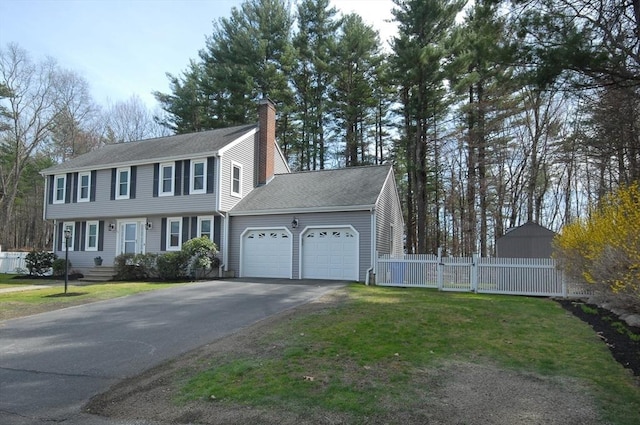 view of front of home featuring a garage, a front lawn, aphalt driveway, fence, and a chimney