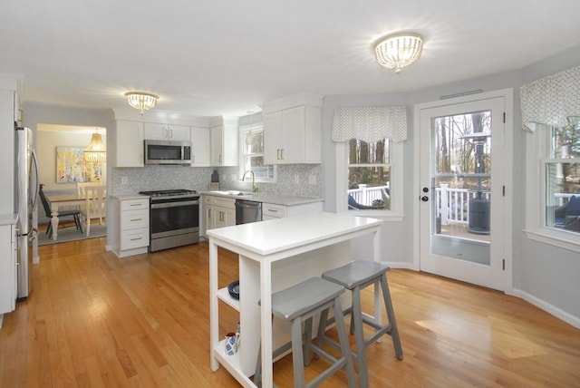 kitchen featuring appliances with stainless steel finishes, white cabinetry, light countertops, a sink, and light wood-style flooring