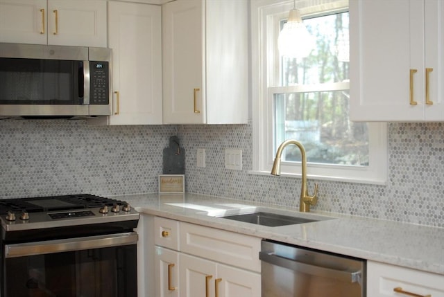 kitchen with decorative backsplash, appliances with stainless steel finishes, light stone countertops, a sink, and white cabinets