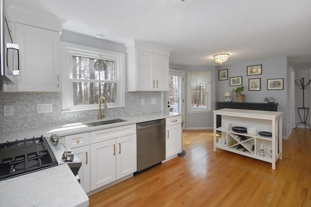 kitchen featuring white cabinets, a sink, light wood finished floors, dishwasher, and tasteful backsplash