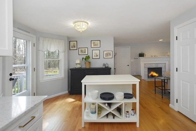kitchen with open shelves, white cabinetry, baseboards, a warm lit fireplace, and light wood-style flooring
