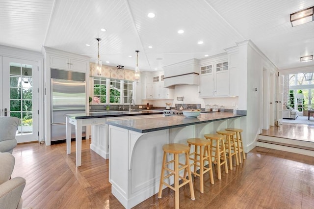 kitchen featuring stainless steel built in refrigerator, white cabinets, light hardwood / wood-style flooring, and hanging light fixtures