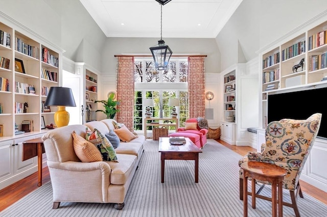 living area with a notable chandelier, light hardwood / wood-style floors, built in features, and a towering ceiling