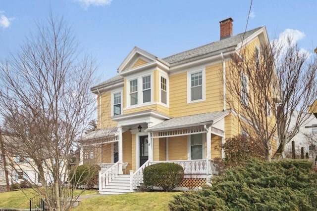 view of front of home featuring a porch, a chimney, a front yard, and a shingled roof