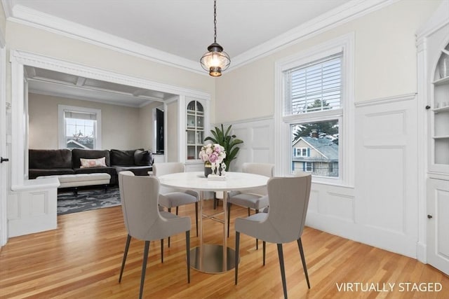 dining room with crown molding, a decorative wall, light wood finished floors, and wainscoting