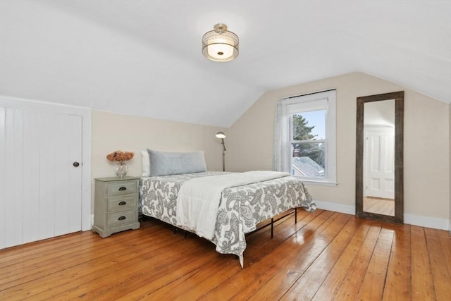 bedroom with baseboards, lofted ceiling, and hardwood / wood-style floors