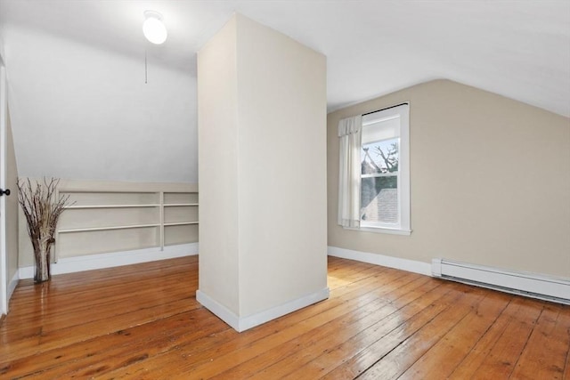 additional living space with vaulted ceiling, a baseboard heating unit, baseboards, and hardwood / wood-style flooring