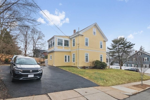 view of side of property featuring a lawn, fence, and a chimney