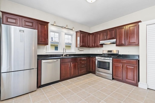 kitchen with dark countertops, under cabinet range hood, appliances with stainless steel finishes, light tile patterned flooring, and a sink