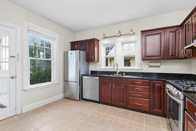 kitchen with dark countertops, baseboards, appliances with stainless steel finishes, and a sink