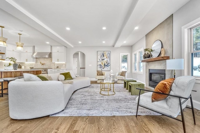 living area with plenty of natural light, light wood-style flooring, arched walkways, and a large fireplace