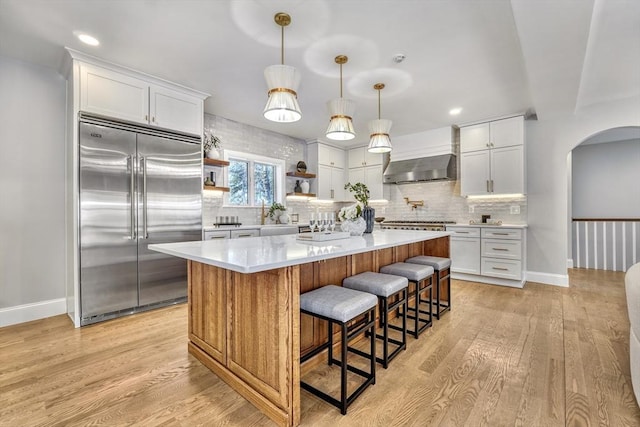 kitchen featuring arched walkways, wall chimney exhaust hood, appliances with stainless steel finishes, and light wood-style flooring