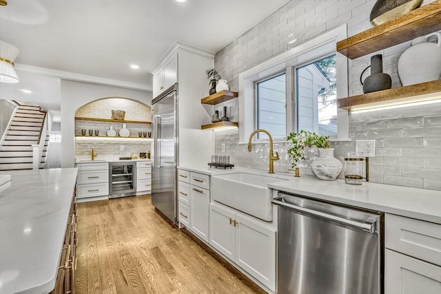 kitchen featuring light wood finished floors, open shelves, appliances with stainless steel finishes, a sink, and beverage cooler