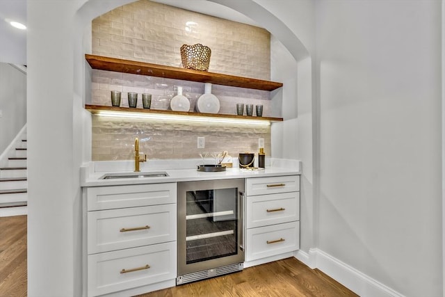 bar with beverage cooler, decorative backsplash, bar, light wood-type flooring, and a sink