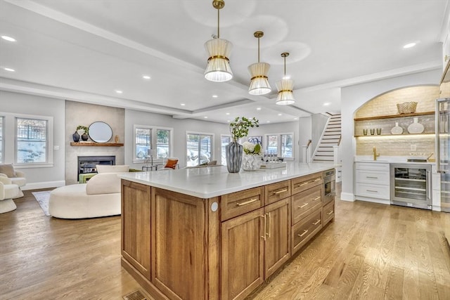 kitchen with beverage cooler, a large fireplace, open floor plan, brown cabinets, and light wood finished floors