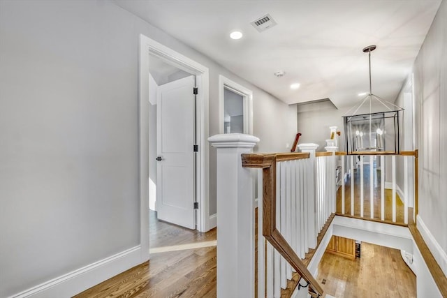 hallway featuring baseboards, visible vents, wood finished floors, an upstairs landing, and a chandelier