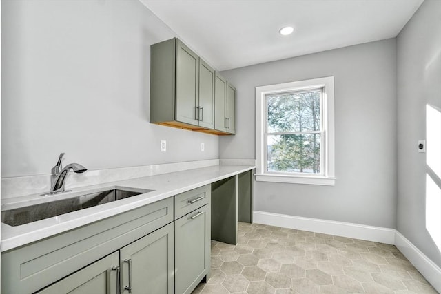 kitchen featuring green cabinets, baseboards, light countertops, and a sink