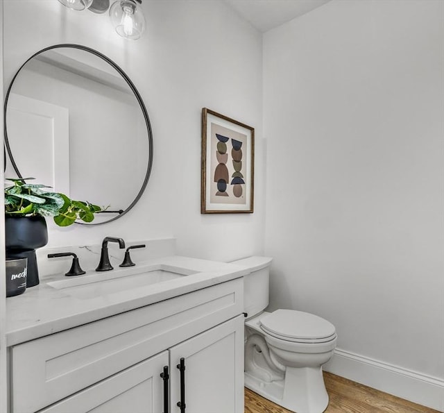 bathroom with toilet, baseboards, wood finished floors, and vanity