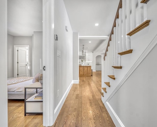 corridor featuring arched walkways, stairway, wood finished floors, and baseboards