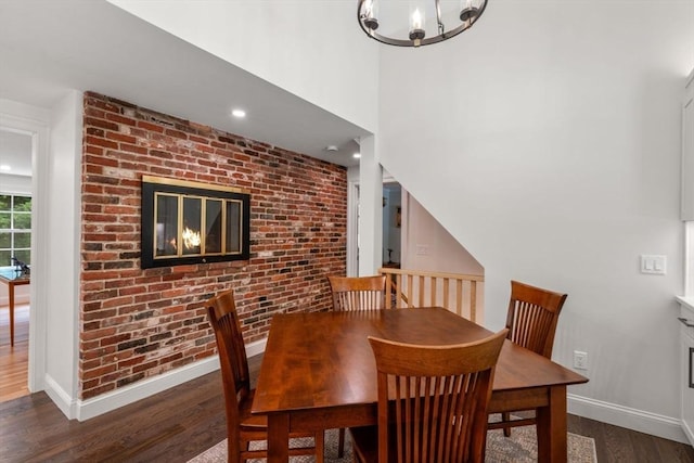 dining space with brick wall, baseboards, an inviting chandelier, and wood finished floors