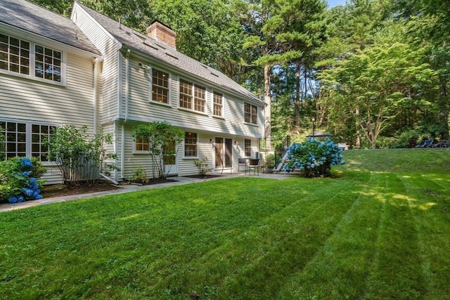 back of house featuring a lawn, a chimney, and a patio area