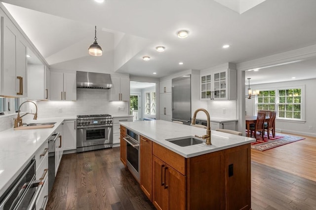 kitchen featuring wall chimney range hood, a center island with sink, appliances with stainless steel finishes, and a sink