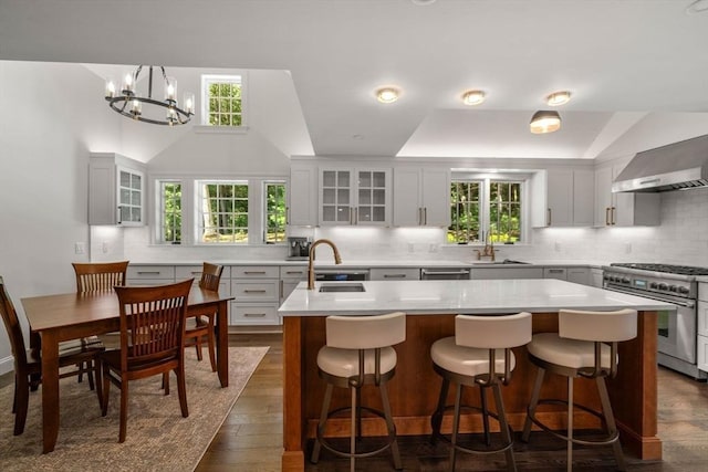 kitchen featuring tasteful backsplash, wall chimney range hood, light countertops, stainless steel stove, and a sink