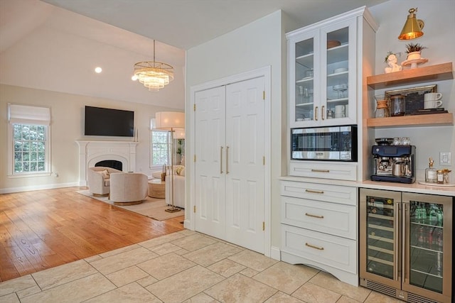 kitchen featuring hanging light fixtures, stainless steel microwave, white cabinets, and beverage cooler