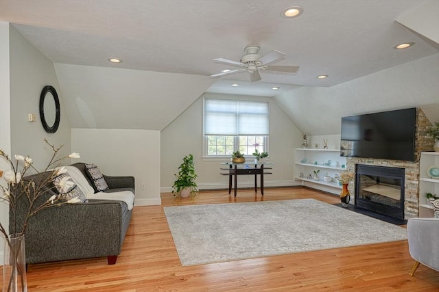 living room with ceiling fan, lofted ceiling, a stone fireplace, and light hardwood / wood-style flooring