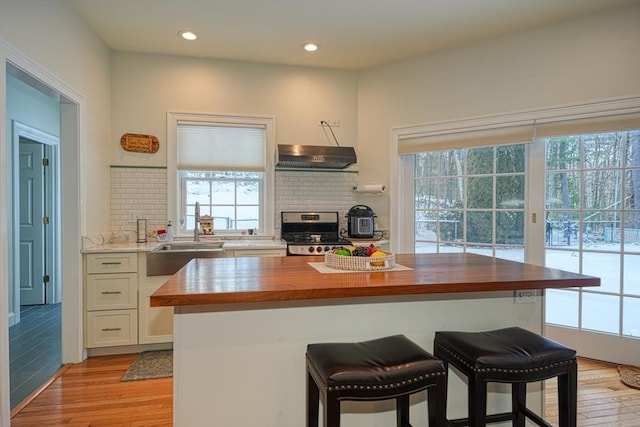 kitchen featuring white cabinetry, backsplash, stainless steel stove, and butcher block countertops