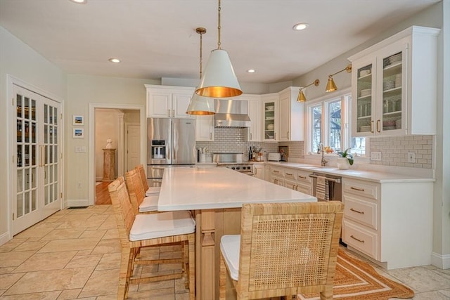 kitchen with decorative light fixtures, a kitchen island, stainless steel appliances, decorative backsplash, and wall chimney range hood