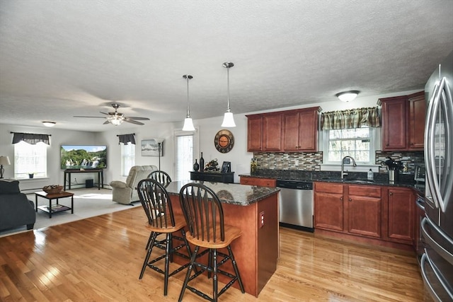 kitchen with a kitchen island, appliances with stainless steel finishes, decorative light fixtures, sink, and a kitchen bar