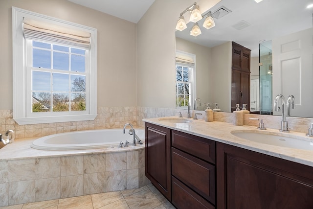 bathroom featuring vanity with extensive cabinet space, a healthy amount of sunlight, tiled tub, tile flooring, and dual sinks